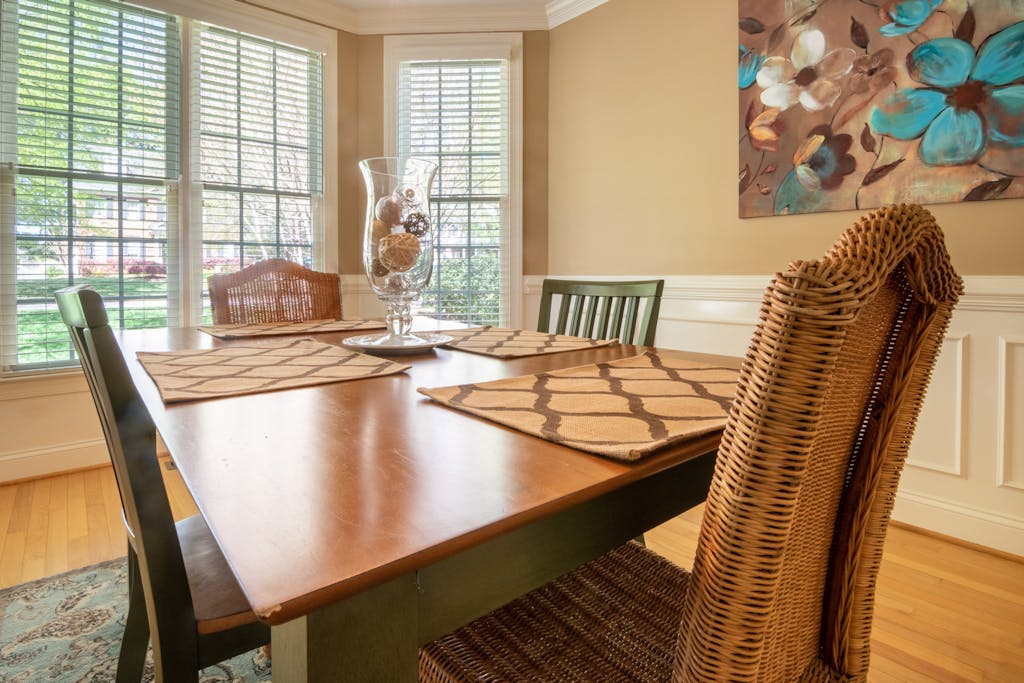 Warm dining room with wooden table, rattan chairs, and decorative vase in natural light.